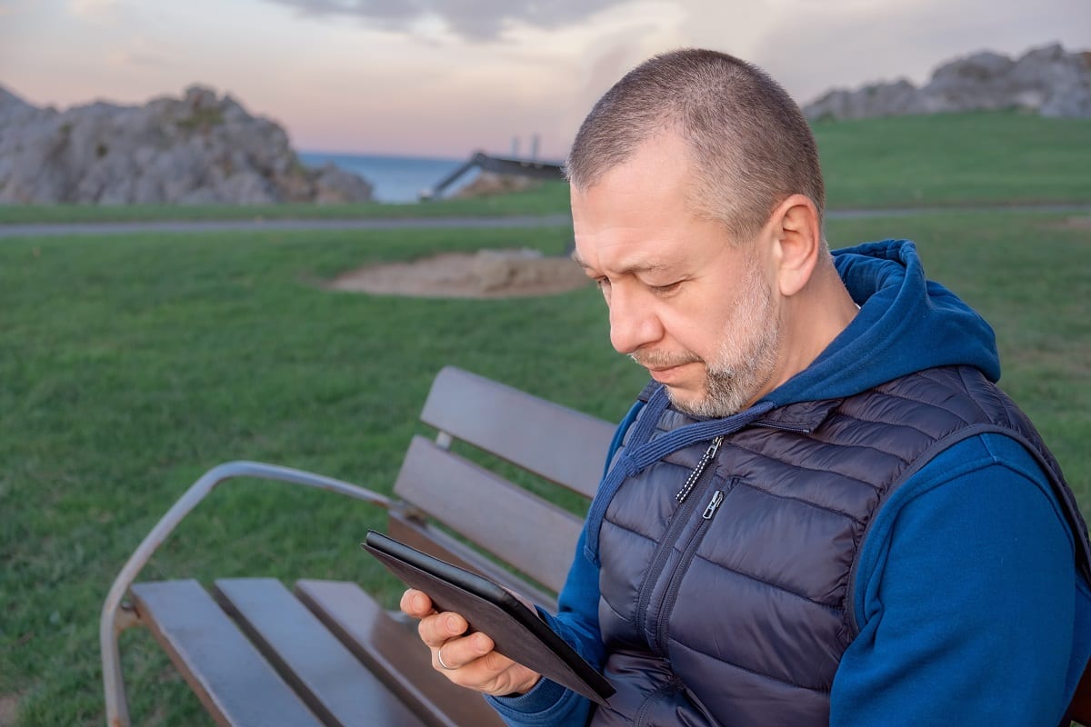 Mature man sits on a Park bench and reads on a digital tablet Man reading tablet